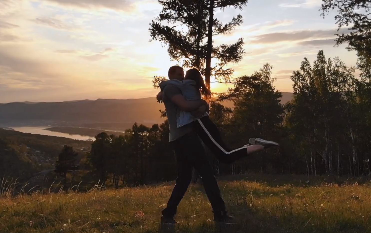 A man twirling his girlfriend in nature, enjoying a splendid time together with a beautiful sunset in the background.