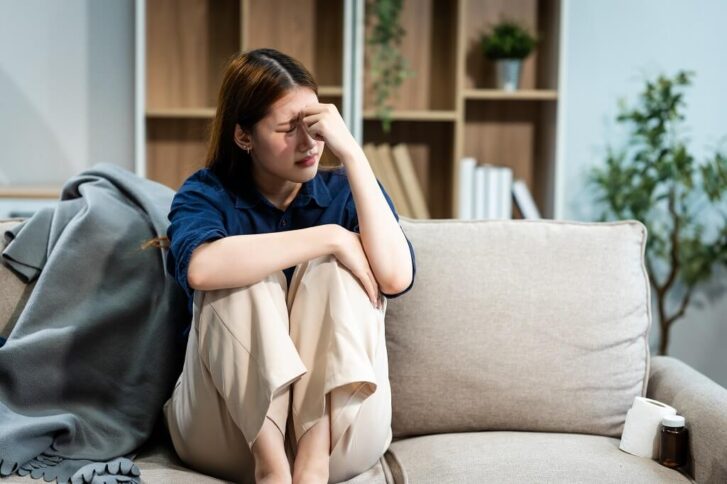 Woman sitting on a couch looking stressed while reflecting on mood symptoms and mental health challenges