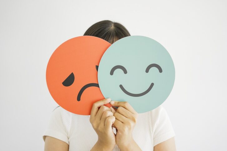 Person holding two face icons showing happy and sad emotions representing mood swings in bipolar disorder