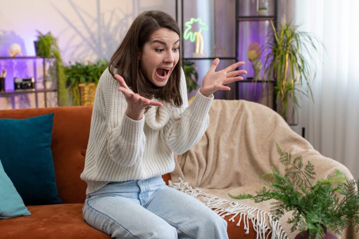 Woman reacting with sudden fear and shock while experiencing overwhelming panic symptoms at home