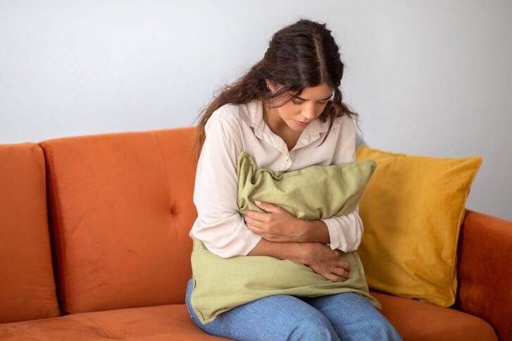 Woman sitting on a couch holding her stomach and feeling nausea and discomfort linked to anxiety or panic