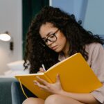Young woman writing in a notebook at home as part of a reflective mental health self-care routine.