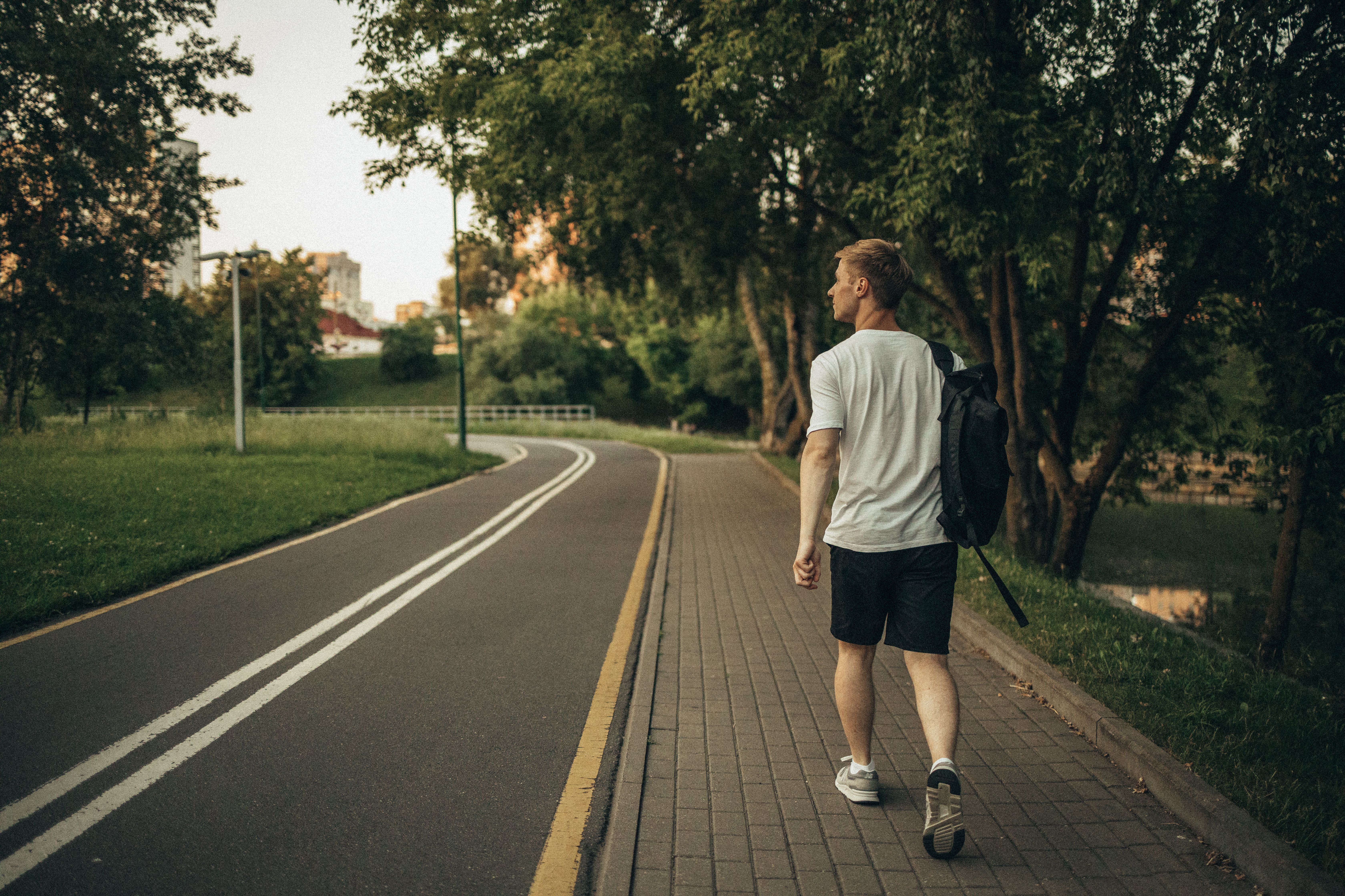 Man walking along a tree-lined park path as a simple outdoor mental wellness activity.